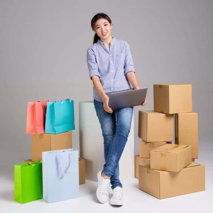 A woman with a laptop and boxes sitting on a white background.