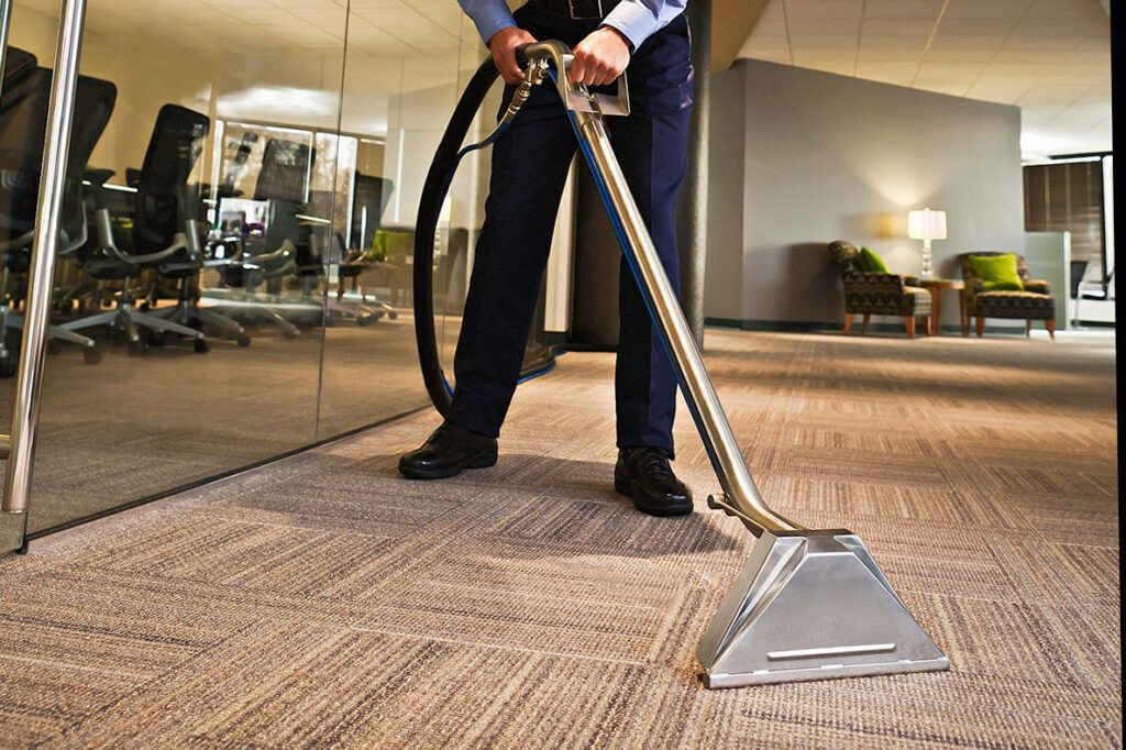 A man is vacuuming a carpeted floor.