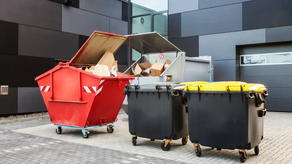 Three garbage cans and a cart are sitting in front of a building.